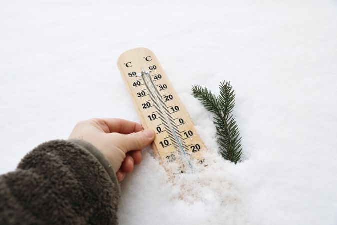 Closeup of womans hand in fleece sweatshirt holding thermometer showing a temperature in Celsius degrees below zero