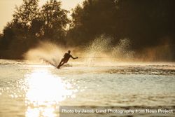 Man water skiing at sunset with one hand on tow rope 48ooY5