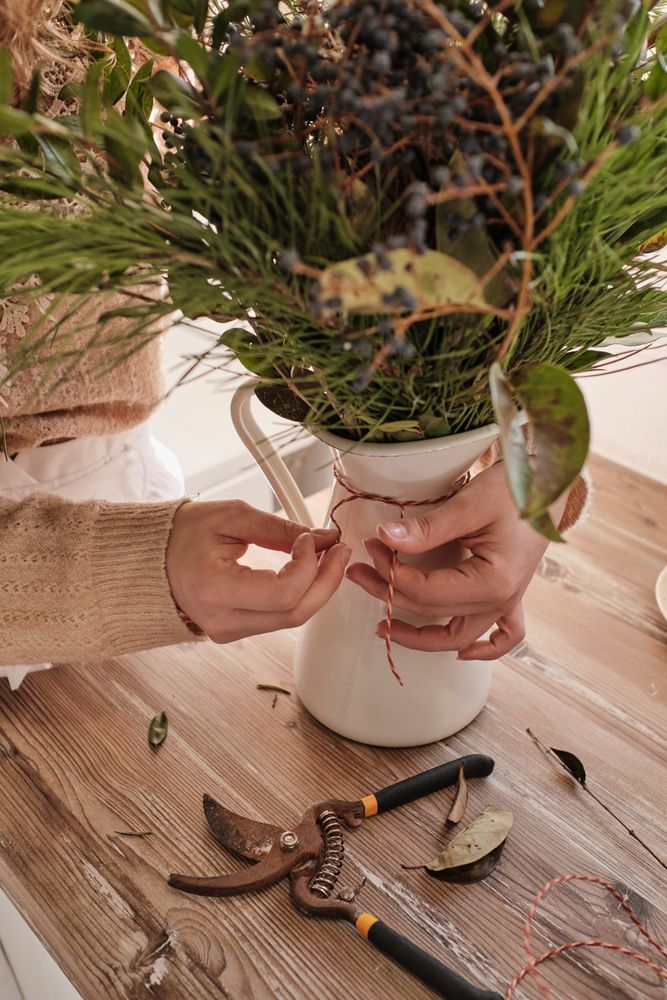 Faceless florist working with bunch of twigs arranged in vase
