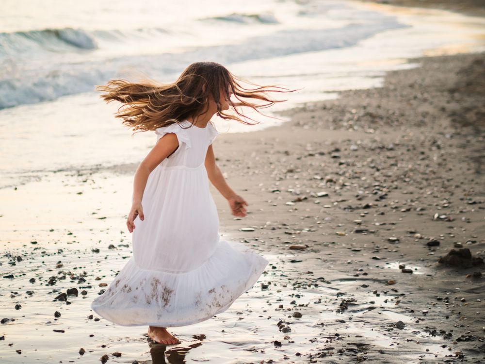 Adorable girl walking and playing on seaside at sunset