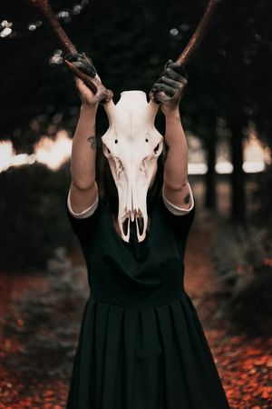 Woman in dark dress holding horse skull with horns