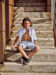 Boy sitting on skateboard on stairs of building