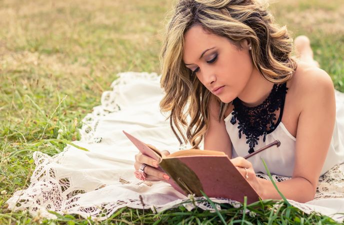 Romantic woman writing in a diary lying down outdoors