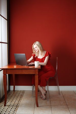 Young adult woman sitting at the table and working on laptop