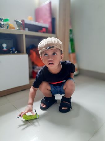 Little boy squatting to pick up toys, playing at home