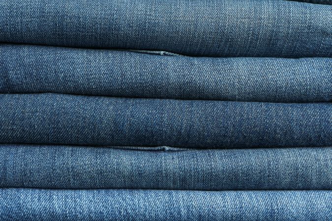 Stack of jeans pants textured background, close up