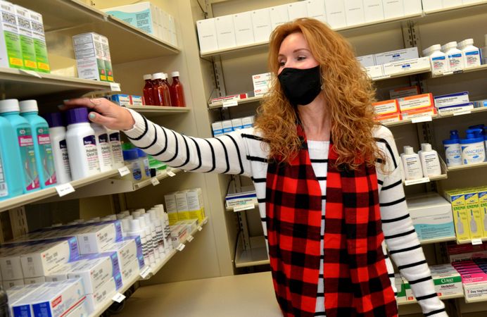 Jacksonville, FL - USA, Dec 1, 2020: Pharmacist wearing facemark reaching for medication on shelf
