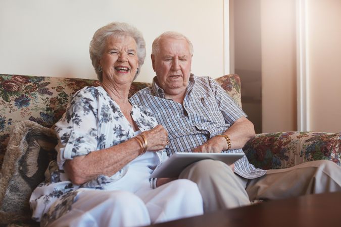 Portrait of smiling older woman sitting with her husband using digital tablet