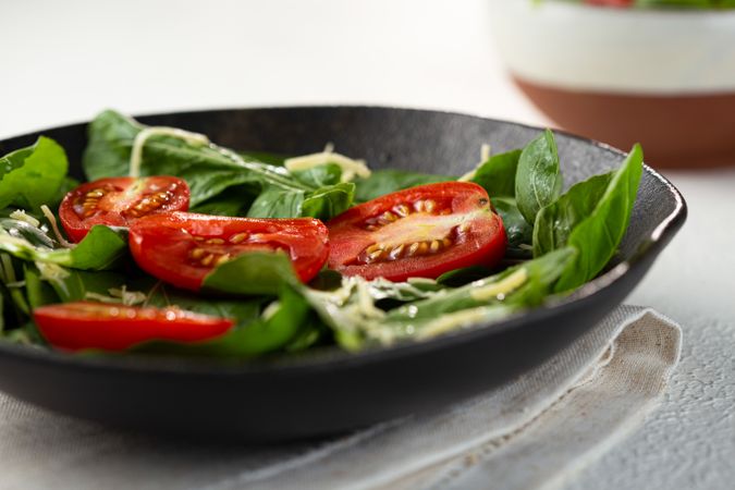 Side view of tomato and spinach salad served in dark bowl with napkin