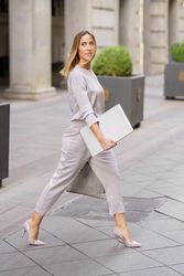 Self assured female manager with laptop crossing street near building