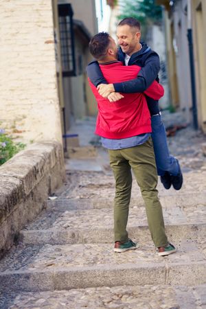 Male lifting up his male partner in cute moment in narrow Spanish street