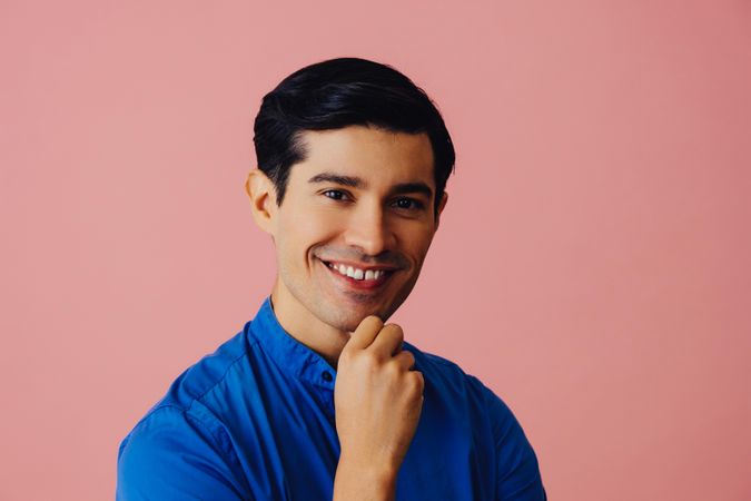 Latino man smiling at camera in pink studio with hand on chin