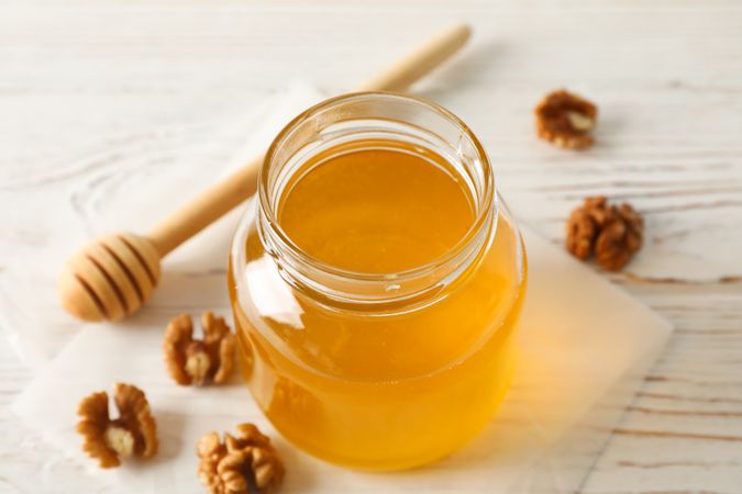 Walnuts, dipper, parchment and glass jar with honey on neutral background, closeup