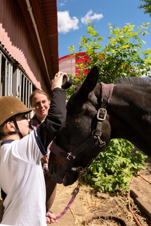 Child gently touches horse's forehead, guided by an adult