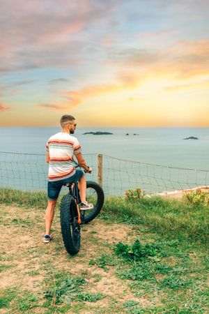 Male standing with bicycle looking down at beautiful ocean view, vertical composition