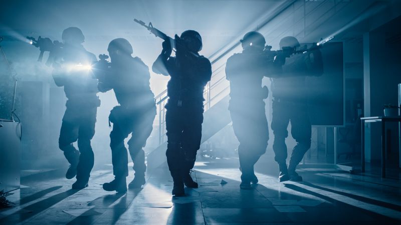 Masked Team of Armed SWAT Police Officers Move in a Hall of a Dark Seized Office Building with Desks and Computers.