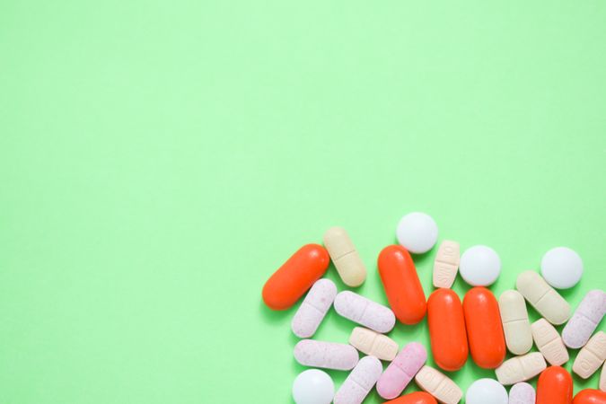 Top view of variety of prescription pills and vitamins on green table with copy space