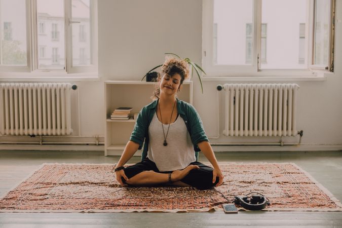 Peaceful woman meditating in lotus position on floor at home