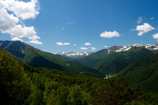 Snow-capped mountains and lush green valleys under blue sky.