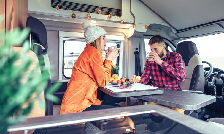Male and female friend enjoying breakfast rolls and sipping coffee in back of van