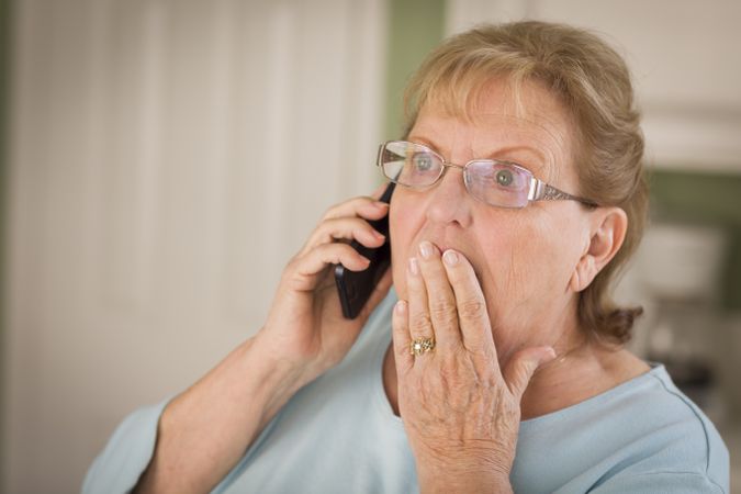 Shocked Older Adult Woman on Cell Phone in Kitchen