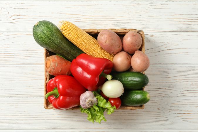 Wicker basket with vegetables on wooden background, copy space