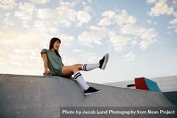 Smiling woman sitting on skateboard ramp in skate park 4N1X25