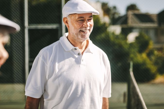 Cheerful mature man standing on a tennis court on a sunny day