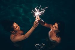 Cheerful friends burning sparkles near pool