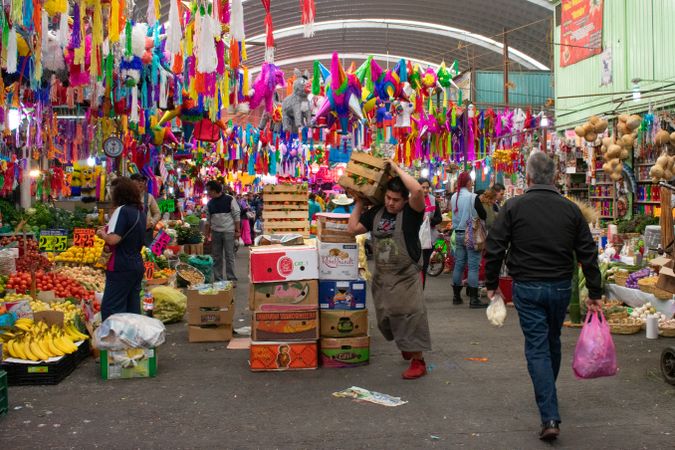 People walking at a market with piñatas hanging from the roof