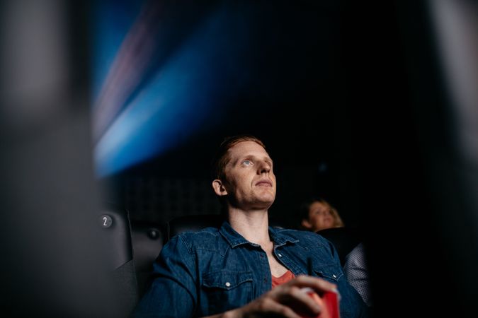 Young man watching movie in cinema with people sitting around