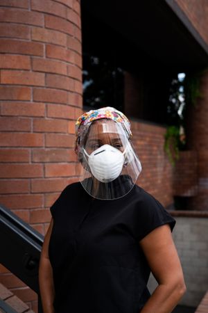 Portrait of Black female nurse in black scrubs, face mask and N95 standing in front of hospital