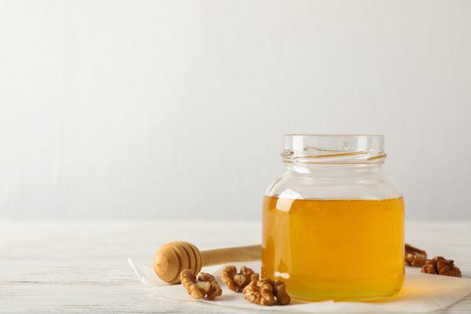 Walnuts, dipper, parchment and glass jar with honey on neutral background, copy space