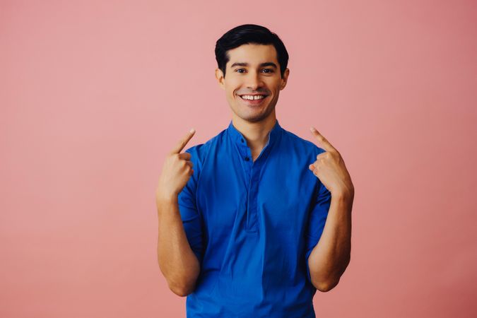 Medium shot of smiling Latino man in pink studio looking up and pointing both fingers at his face