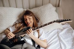 Young brunette woman playing guitar on bed