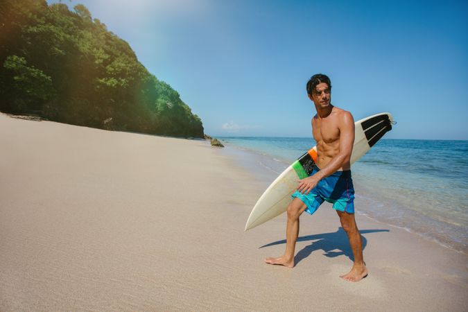 Male surfer holding surf board walking out of the sea