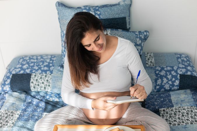Pregnant woman having breakfast and taking notes in notepad