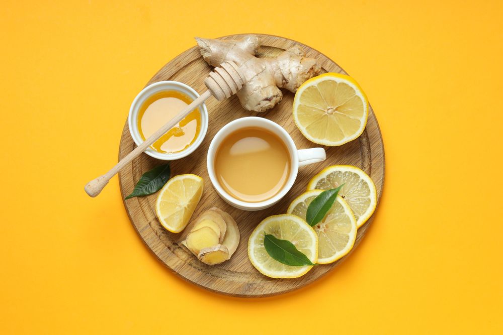 Cup with tea, lemon, ginger and honey on yellow background, top view
