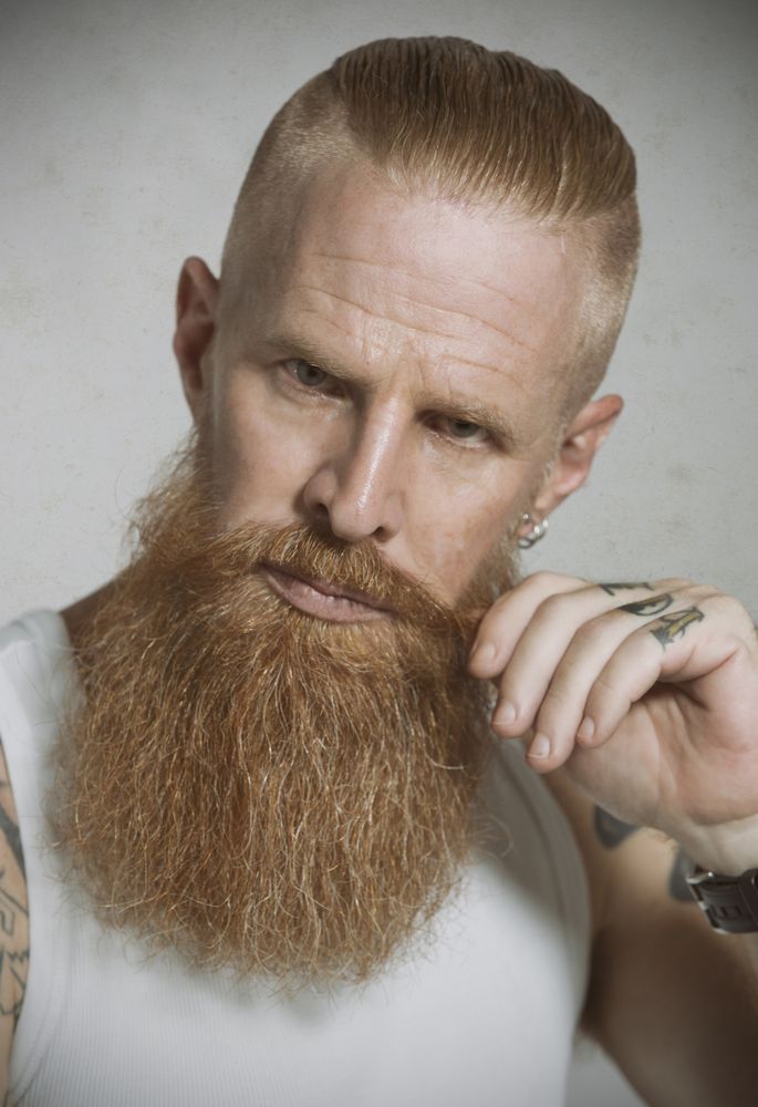 Confident adult red haired hipster tightening mustache and looking at camera