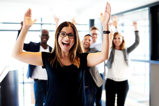 Businesswoman pictured in a bright office in front of her colleagues with their arms in the air