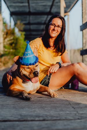 Casual young woman resting next to brown dog with party hat