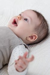 Happy baby girl lying on back over white bedcover