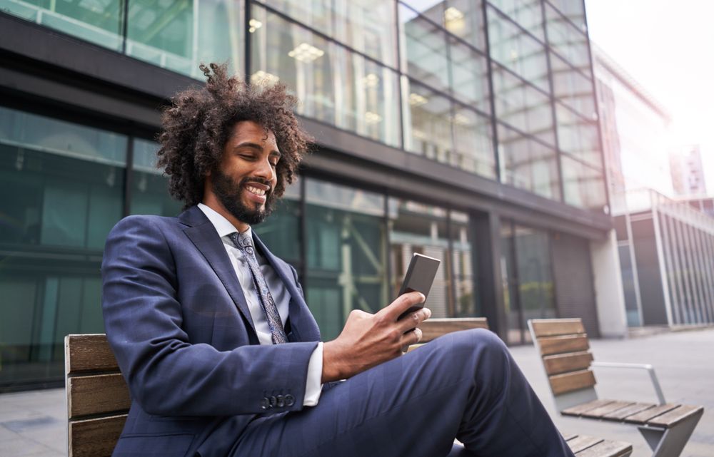 Joyful man in suit sitting outside and messaging