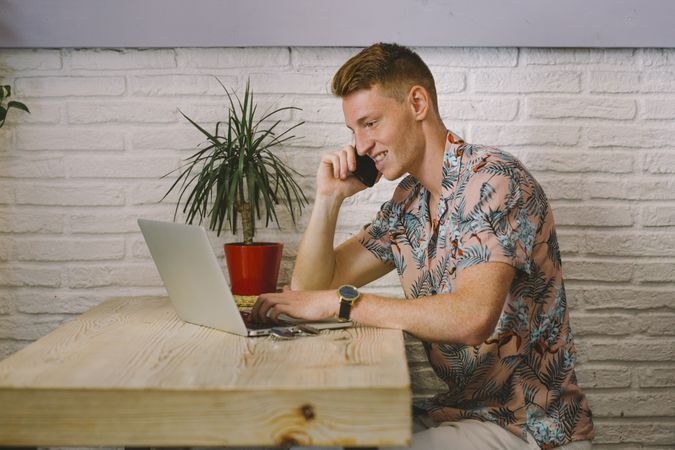 Man talking on smartphone while browsing laptop