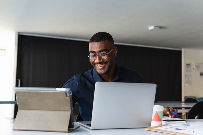 Black guy video chatting on tablet near laptop in workplace