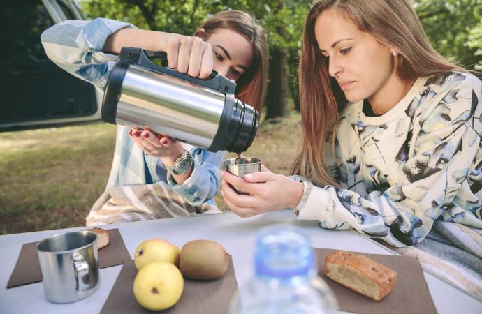 Woman pouring coffee in cup to friend