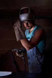 Man in helmet and welding gloves in dark workshop