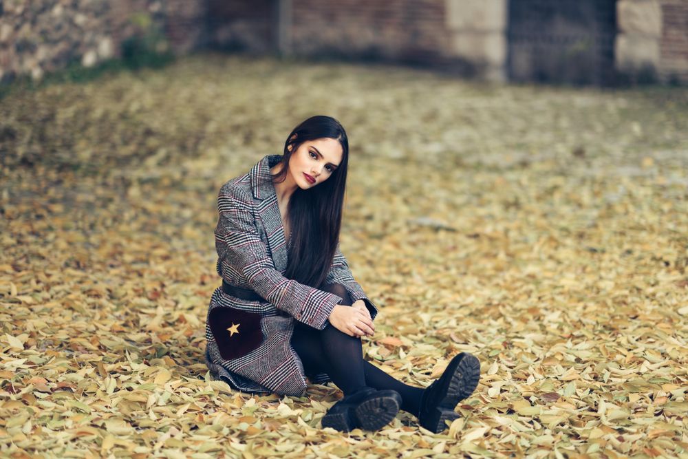Content female relaxing in park in fall time with colorful leaves on ground looking at camera