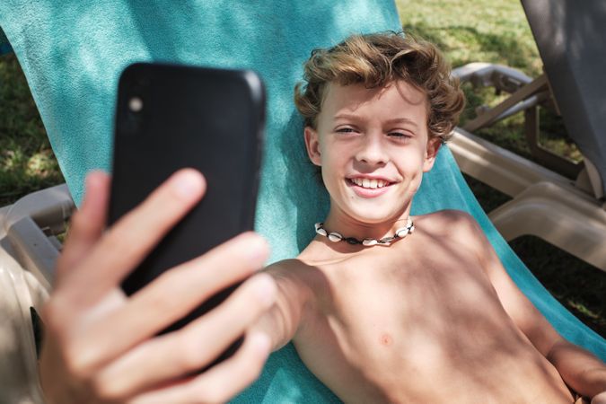 Cheerful boy taking selfie on smartphone in resort garden
