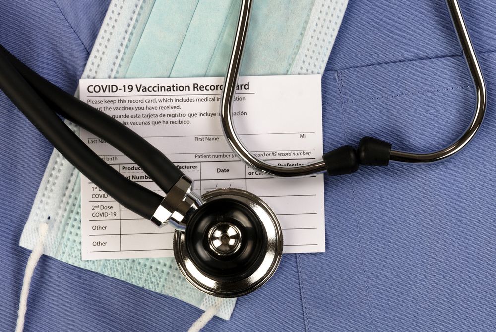 Covid 19 vaccination record card, personal facemask and stethoscope on blue medical outfit in close up view